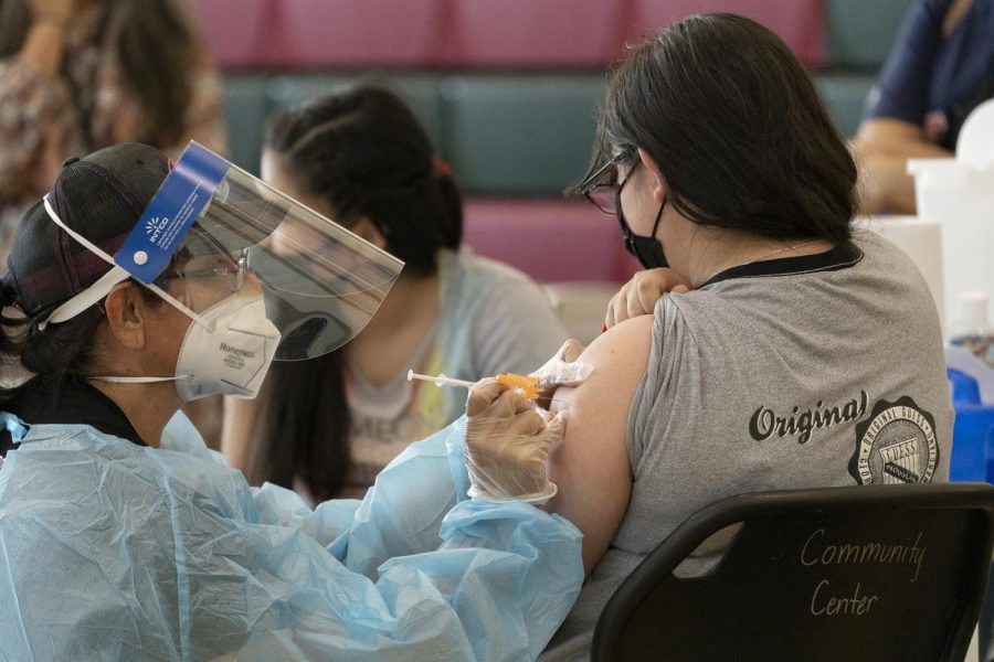 FILE - In this May 27, 2021, file photo, sisters Guadalupe Flores, 15, right, and Estela Flores, 13, left, from East Los Angeles, get vaccinated with the Pfizer's COVID-19 vaccine by licensed vocational nurse Rita Orozco, far left, at the Esteban E. Torres High School in Los Angeles. The Los Angeles board of education is expected to vote Thursday, Sept. 9, on whether to require all students 12 and older to be fully vaccinated against the coronavirus to participate in on-campus instruction in the nation's second-largest school district. (AP Photo/Damian Dovarganes, File)