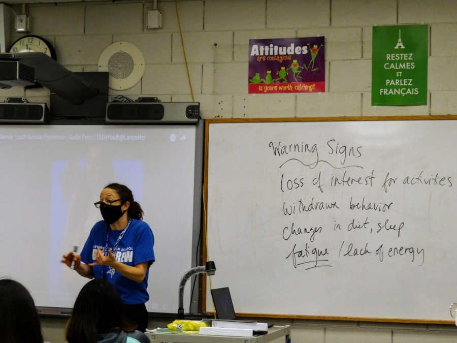 Mrs. Faitel and the peer counselors discuss the video “Shattering the Silence,” in which a teenage girl shares her experience with suicide; the board shows warning signs like withdrawn behavior and lethargy. Displaying one sign occasionally is normal, but people should consider reaching out if they notice someone displaying more than one consistently.