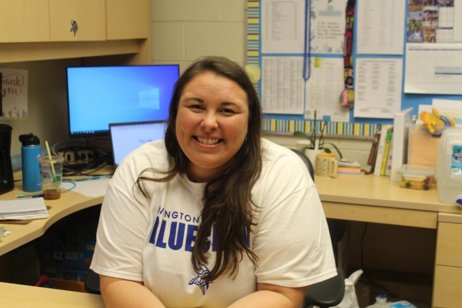 Ms. Tutass poses for a photo in front of her desk.