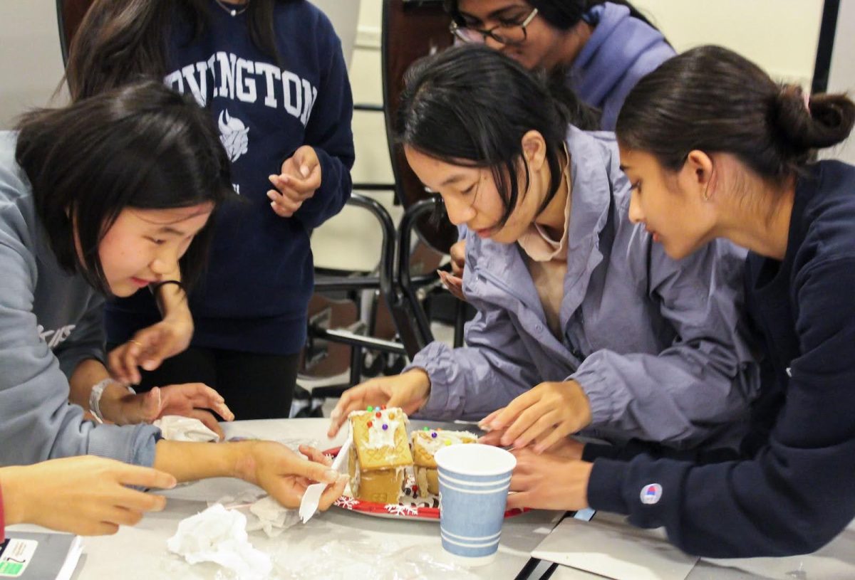 Participants in the gingerbread house-making event focus intently as they craft their creations with frosting and candy.